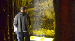 Descrição da imagem: Representação do interior de uma caverna, onde duas pessoas estão observando as estruturas.