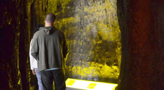 Descrição da imagem: Representação do interior de uma caverna, onde duas pessoas estão observando as estruturas.