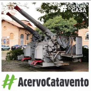 Foto de um Canhão exposto na área externa do Museu Catavento. Ao fundo algumas arvores e uma estrutura de blocos