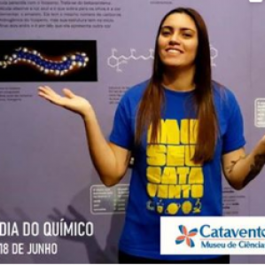 Foto de uma mulher de camiseta azul sorrindo. Ao fundo uma parede roxa com alguns desenhos e escritas