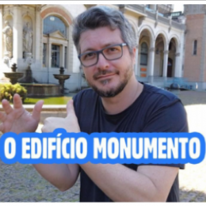 Foto de um homem de camiseta preta e óculos a frente de um palácio fazendo gestos com as mãoes