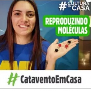 Foto de uma mulher de camiseta azul segurando "moléculas" em sua mão. Ao fundo uma parede azul