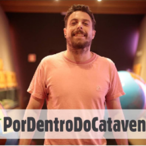Foto de um homem com camiseta laranja sorrindo. Ao lado maquete de globos terrestres.