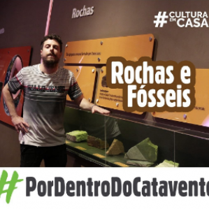Homem com camiseta cinza sorrindo ao lado de algumas rochas e fosseis