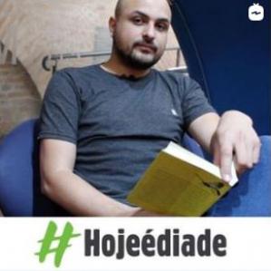 Homem sentando em uma cadeira azul segurando um livro