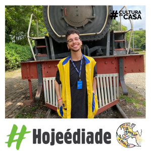Homem sorrindo com colete amarelo, ao fundo uma locomotiva