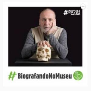 Homem careca no fundo preto e a sua frente um crânio