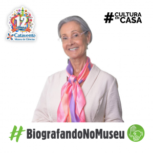 Mulher sorrindo com uma camisa branca e lenço rosa pendurado no pescoço