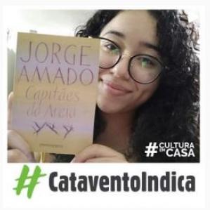 Mulher de cabelos cacheados, óculos redondo, segurando um livro