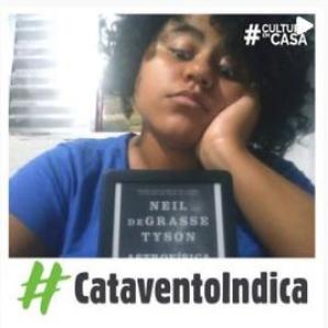Mulher negra de camiseta azul e a frente a capa do livro
